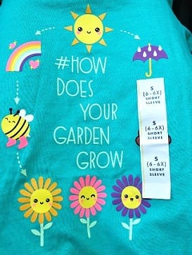 T-shirt That Says "How Does Your Garden Grow" with Graphics of Flowers, Sun, Bee, Rainbow, Umbrella, and a Size Sticker
