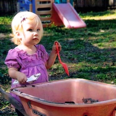 Toddler with a Wheelbarrow and Garden Tools in a Garden