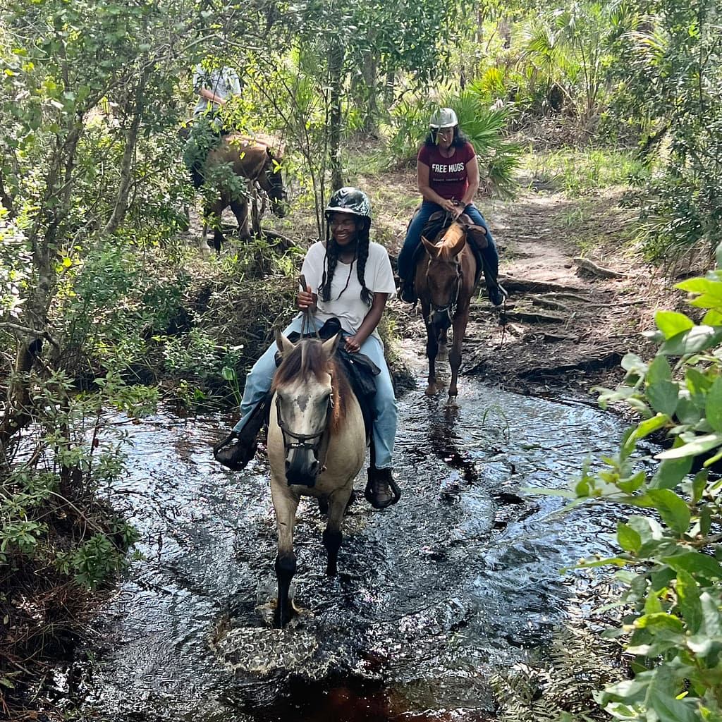 People Riding Horses Through a Creek