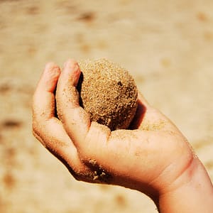 Child's Hand Holding Ball of Sand