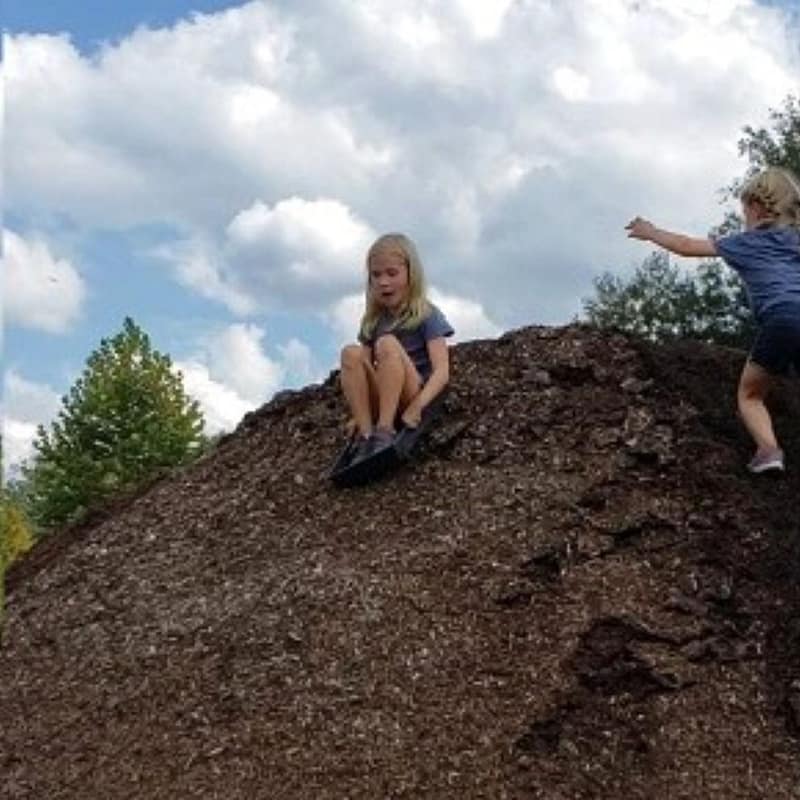 Girl Slides Down Soil Pile While Another Girl Climbs Up the Pile