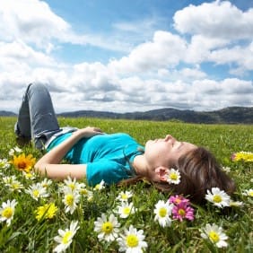 Girl Laying in Meadow Among Flowers, Looking at Blue Sky with Clouds